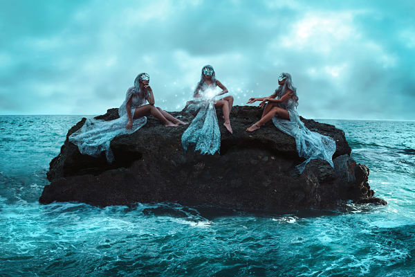 women sitting on rock in ocean 
